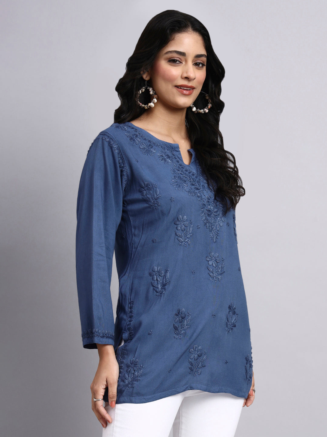 Woman wearing a blue embroidered top against a gray background