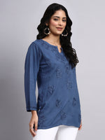 Woman wearing a blue embroidered top against a gray background
