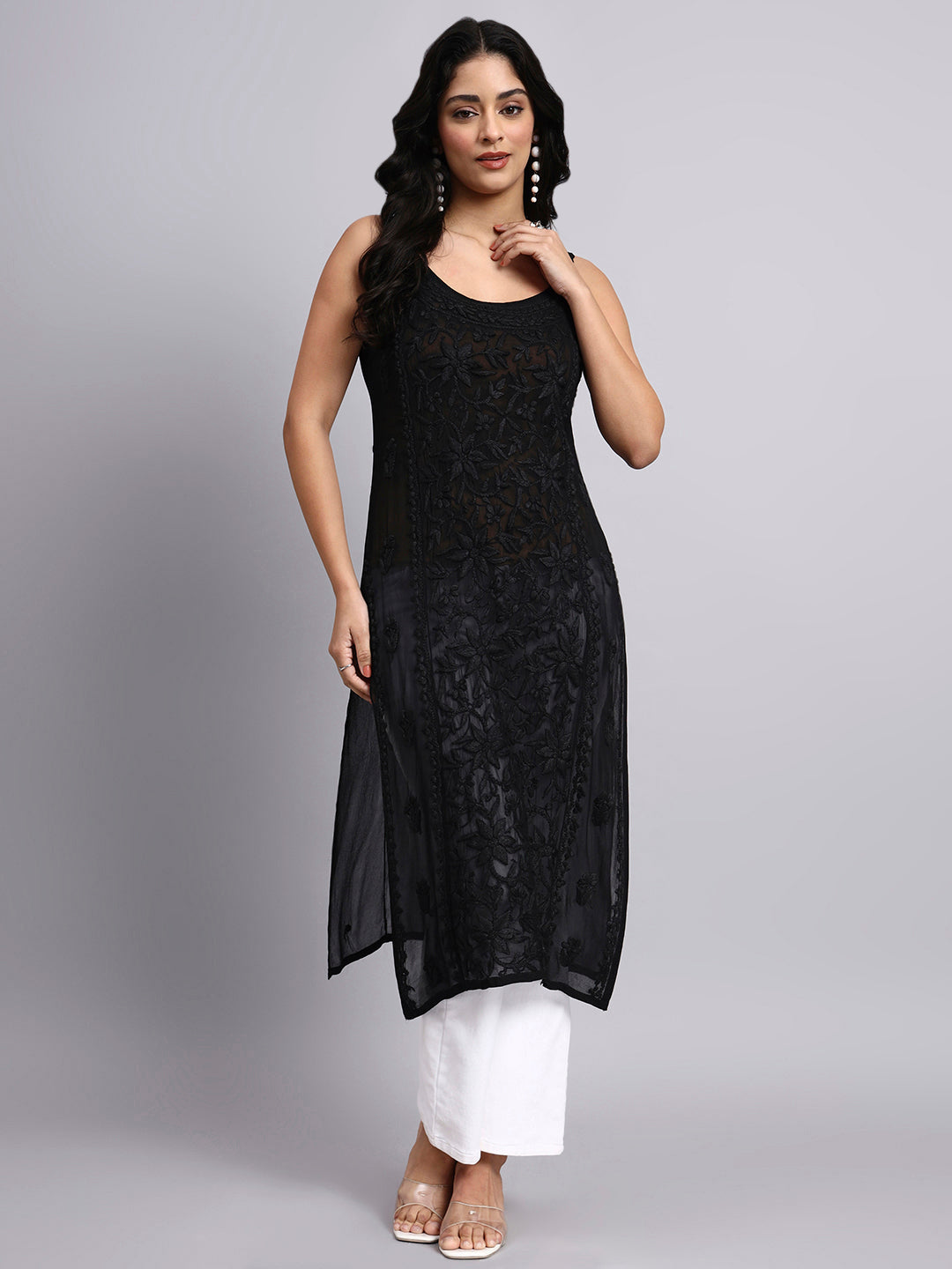 Woman wearing a black sleeveless cotton chikankari kurti with white pants on a gray background