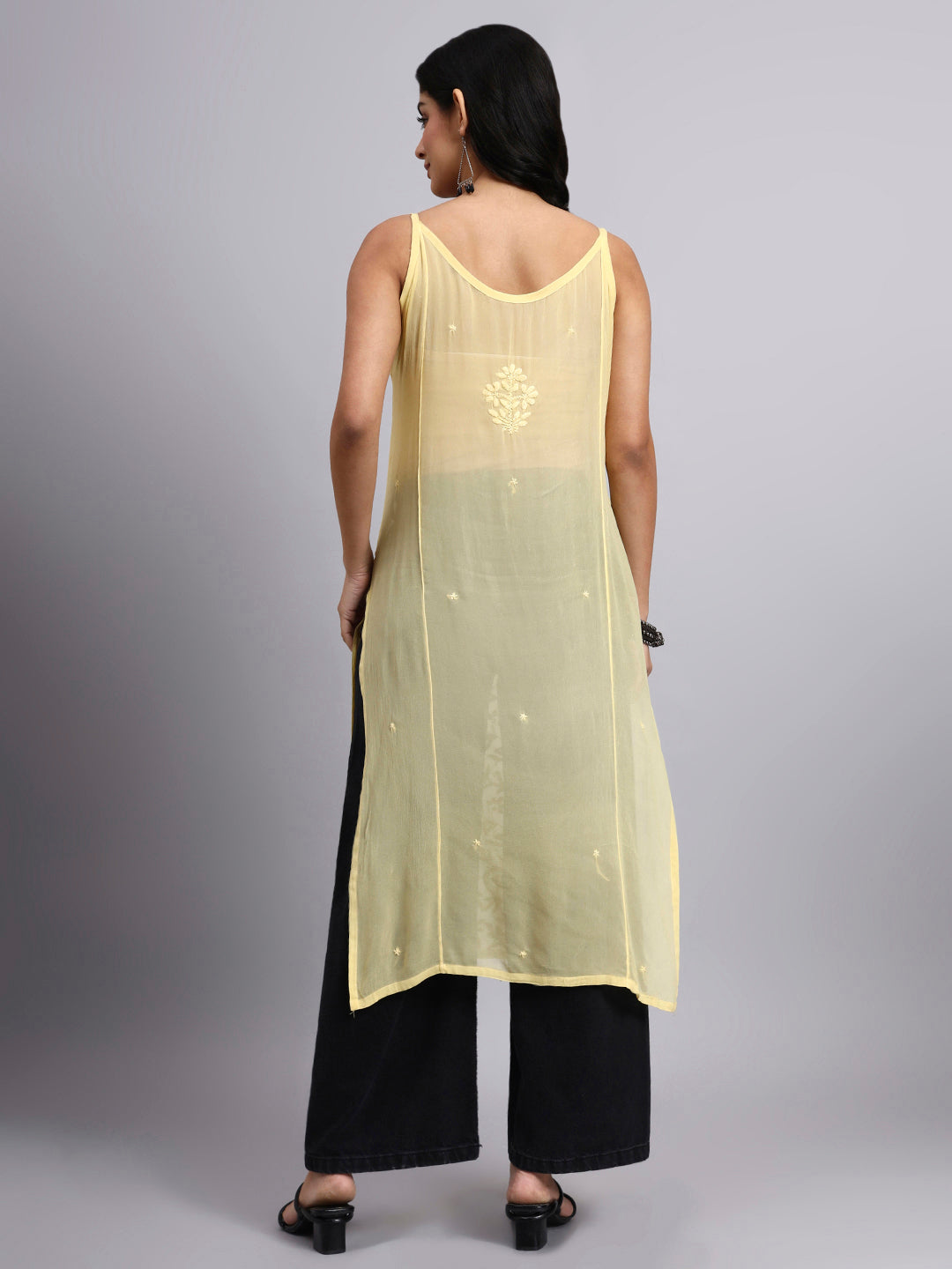 Back view of Woman wearing a light yellow sleeveless top with black pants on a gray background