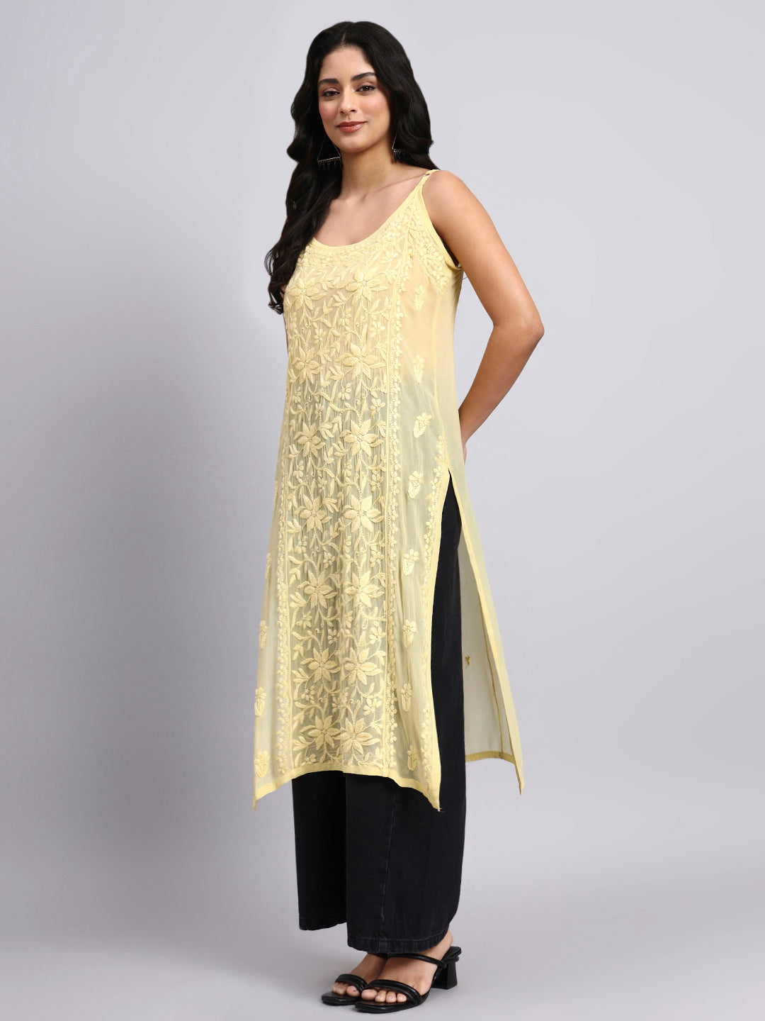 Side angle of Woman wearing a yellow sleeveless top with black pants on a gray background