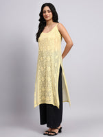 Side angle of Woman wearing a yellow sleeveless top with black pants on a gray background
