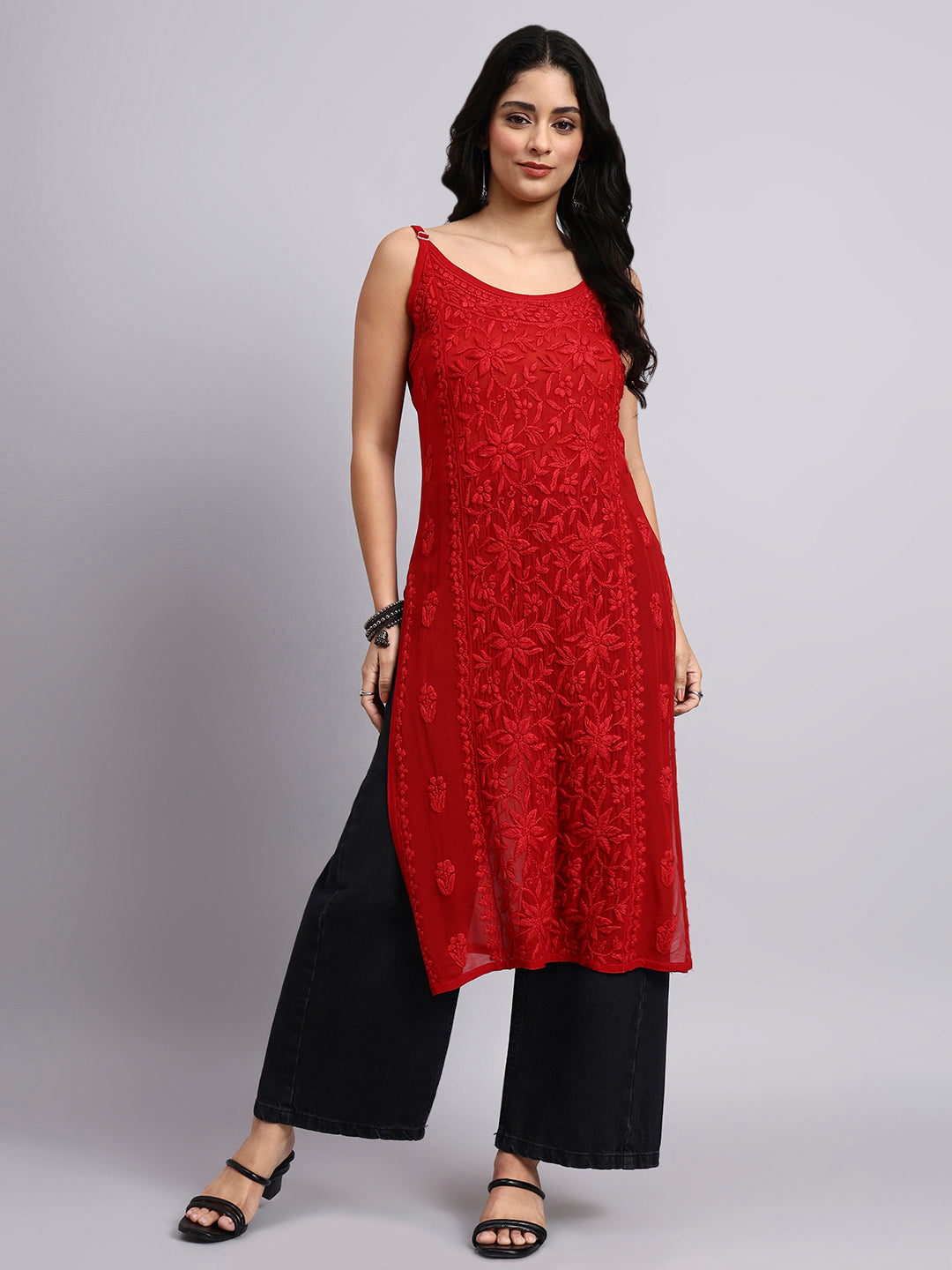 Full view of Woman wearing a red sleeveless chikankari long kurta and black pants on a gray background