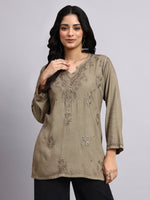 Front view of Woman wearing a olive embroidered top against a gray background