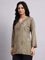 Woman wearing a beige embroidered chikankari kurtaagainst a gray background