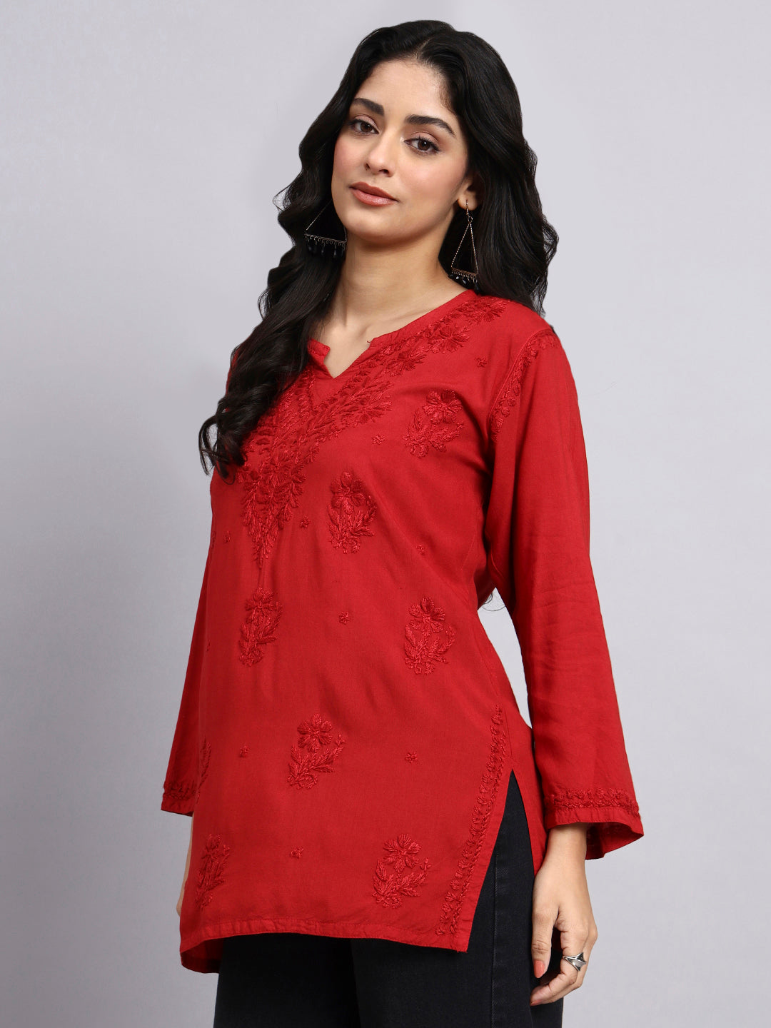 Side view of Woman wearing a red embroidered short kurta against a gray background