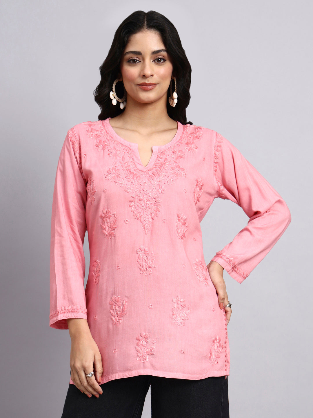 Woman wearing a pink embroidered top against a gray background