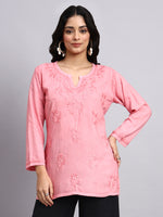 Woman wearing a pink embroidered top against a gray background