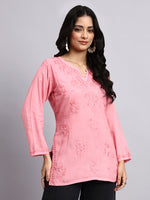 Woman wearing a pink chikankari kurta top against a gray background