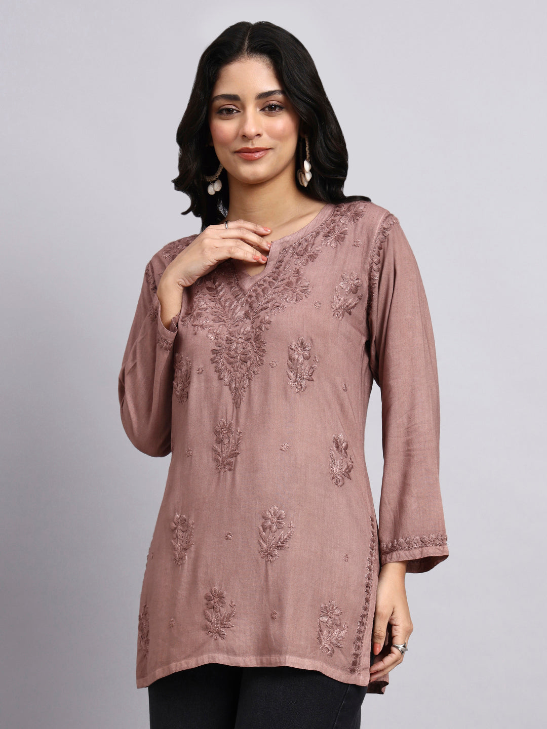 Woman wearing a mauve embroidered top against a plain background