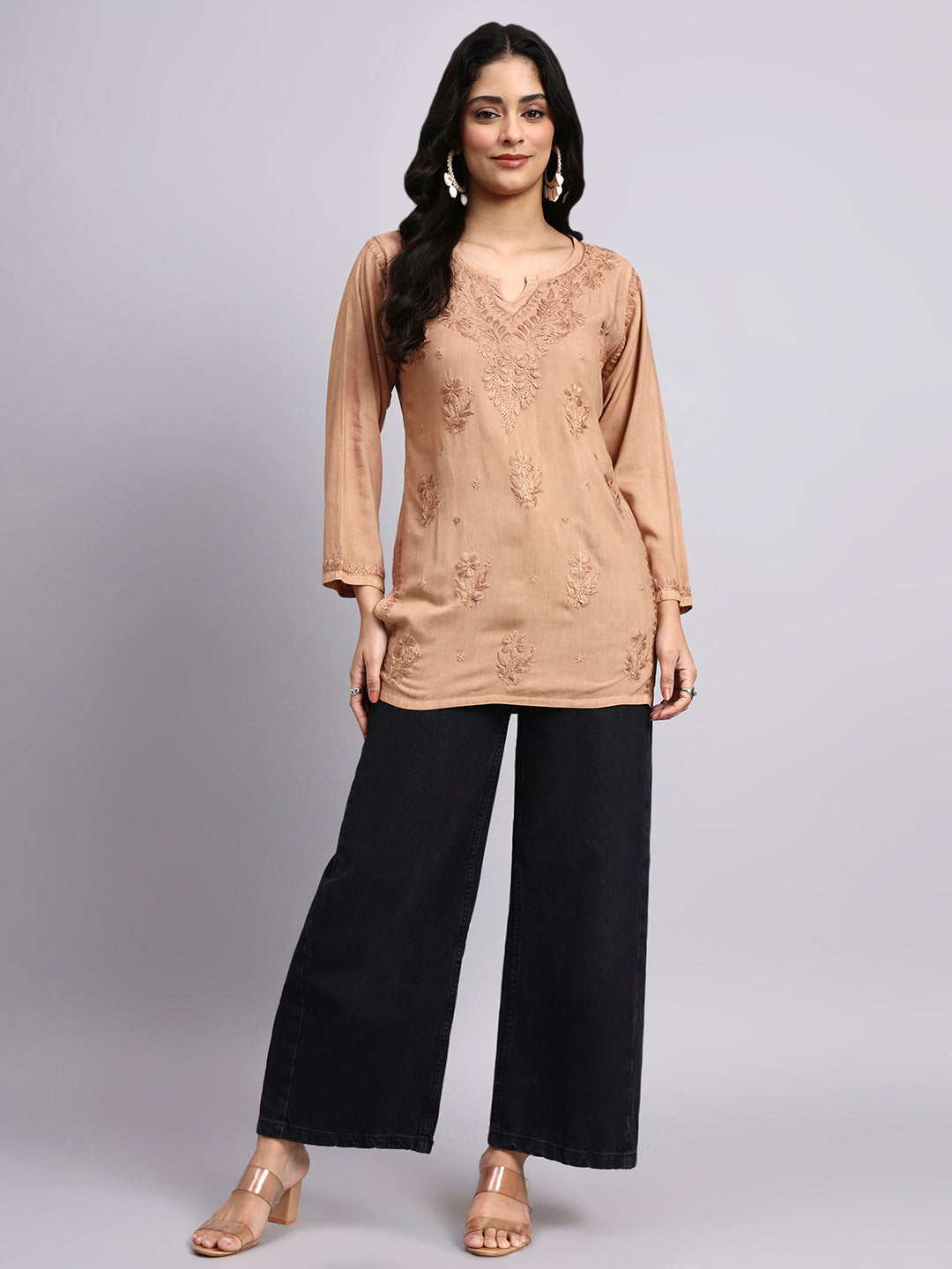 Woman wearing a beige embroidered short kurta and black pants on a gray background