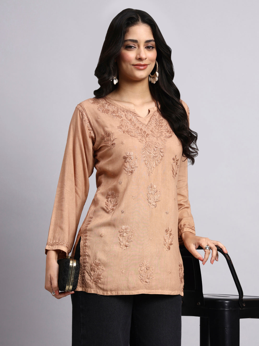 Woman wearing a beige embroidered top with black pants on a gray background