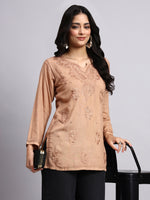 Woman wearing a beige embroidered top with black pants on a gray background