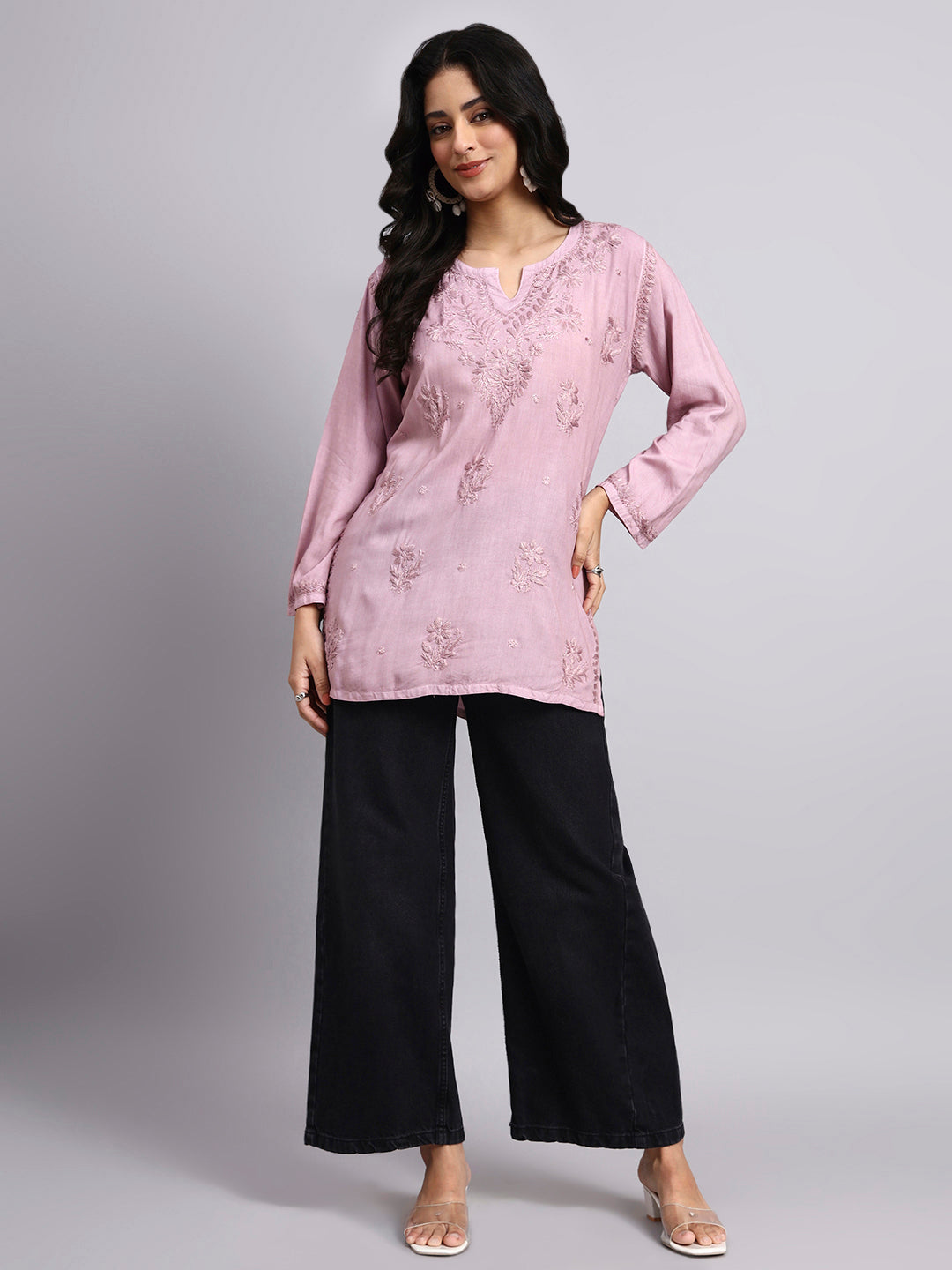 Woman wearing a pink embroidered top and black pants on a gray background